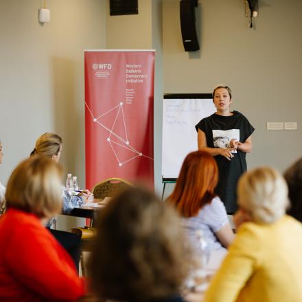 a woman giving a presentation next to a WBDI banner